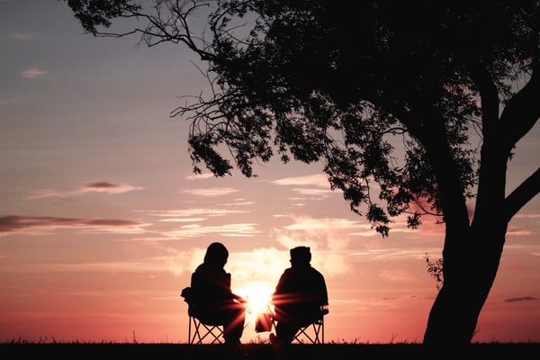 A coach and trainee sitting in front of a pink sunrise.